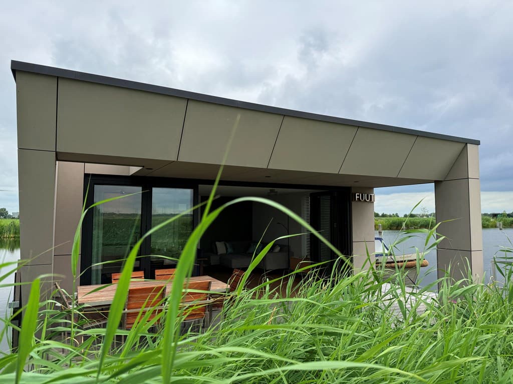 Moderne vakantiewoning aan het water met ruime overkapping en zicht op groen gras en water.