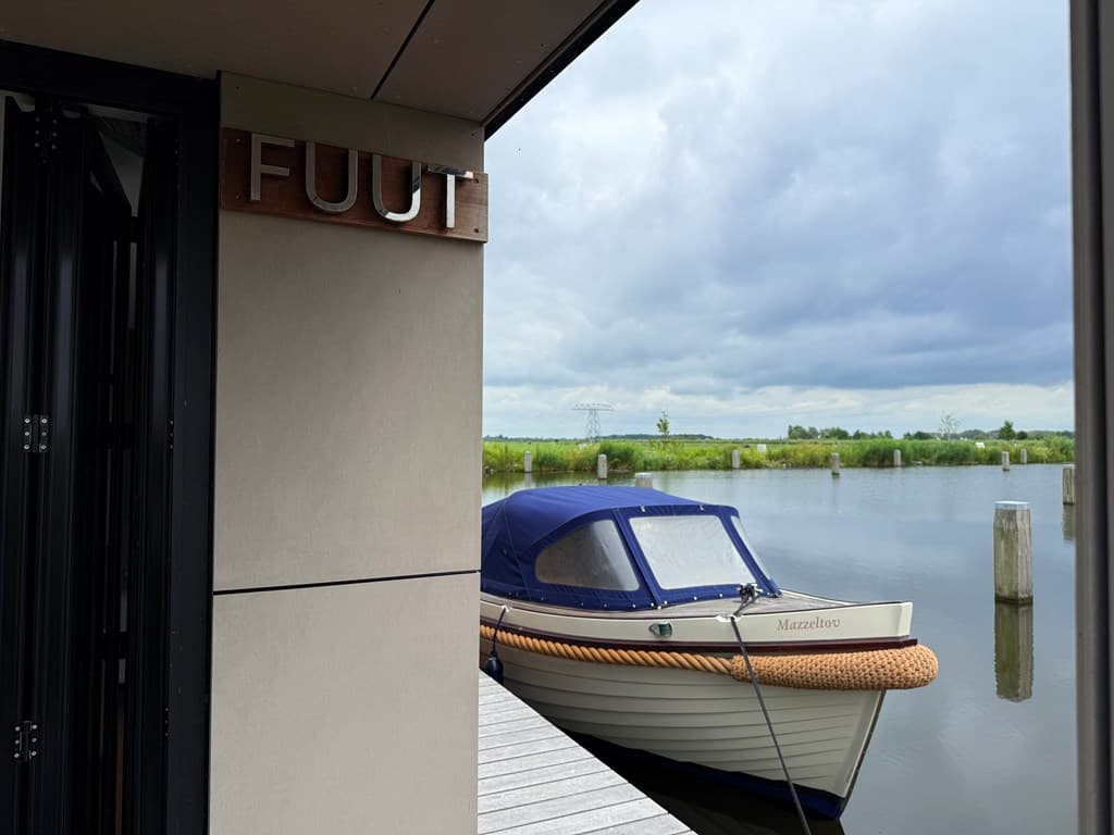 Aanzicht van een steiger met een boot aan de waterkant en een bord met de naam 'Fuut' zichtbaar.