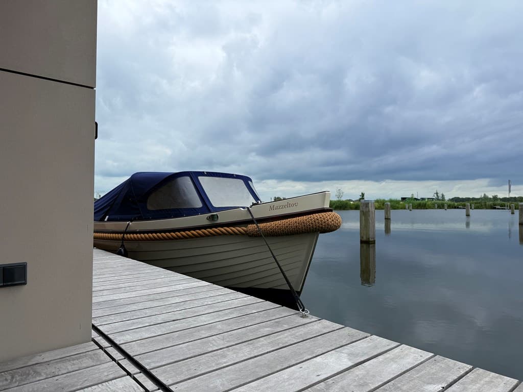 Botensteiger met een motorboot aan het water, rustige omgeving met een bewolkte lucht en riet in de verte.
