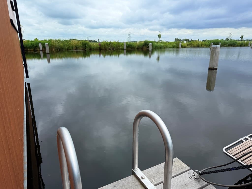 Uitzicht op het water met weerspiegelingen en palen in de achtergrond bij Waterstaete Tjeukemeer.