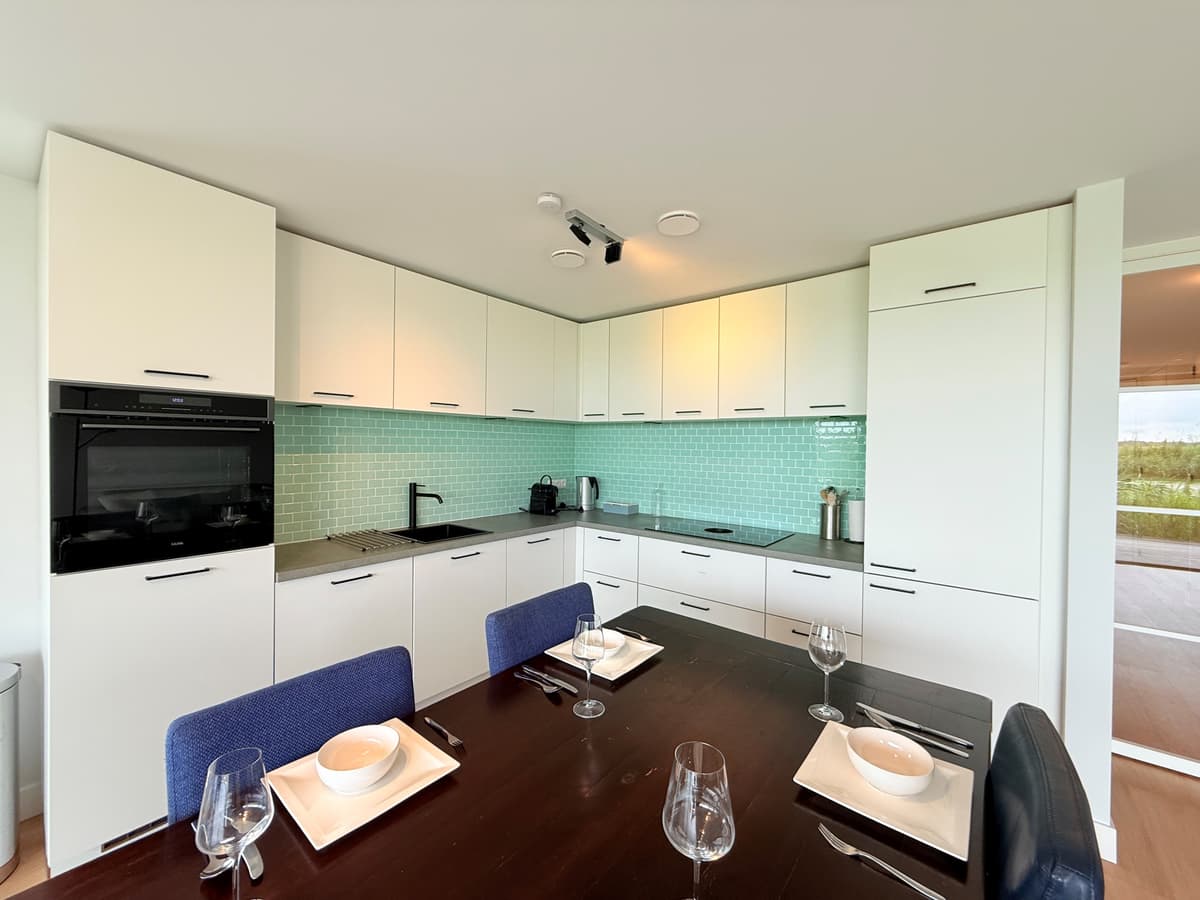 Moderne keuken met groene achterwand, eettafel en vier stoelen, zicht op terras.