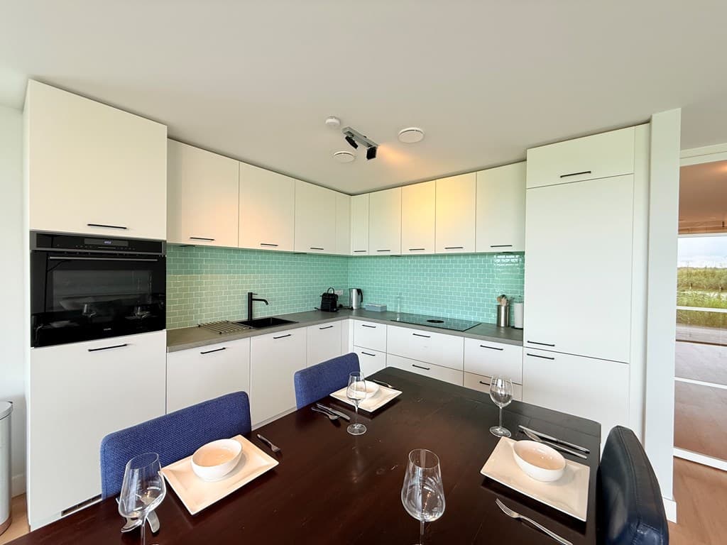Moderne keuken met groene achterwand, eettafel en vier stoelen, zicht op terras.