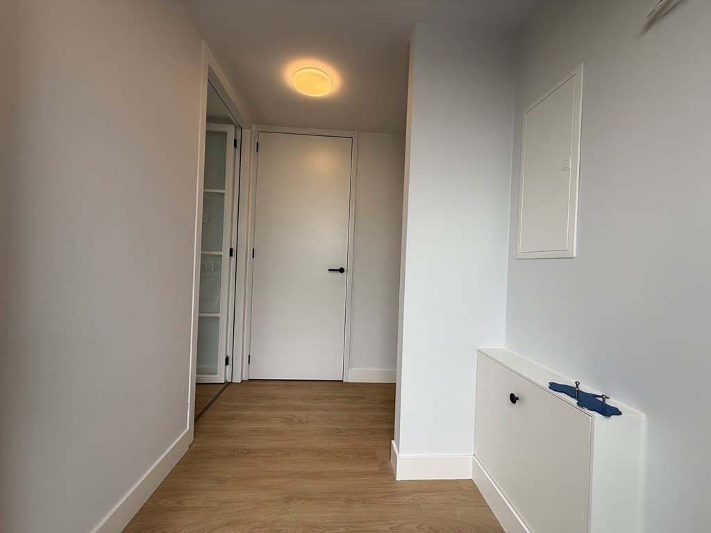 Licht ingerichte hal met moderne vloer, deur naar andere ruimtes en wandkasten.