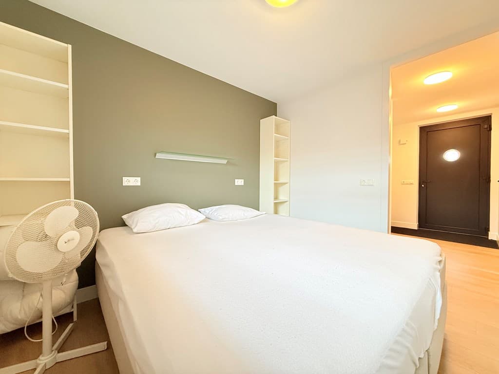 Slaapkamer met tweepersoonsbed, boekenplank en een deur naar de gang