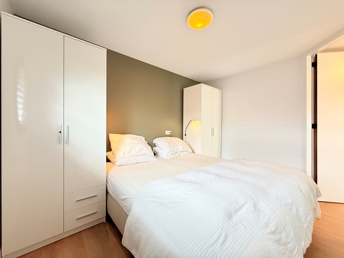 Slaapkamer met tweepersoonsbed, witte kast en zacht verlichte wand in een moderne inrichting