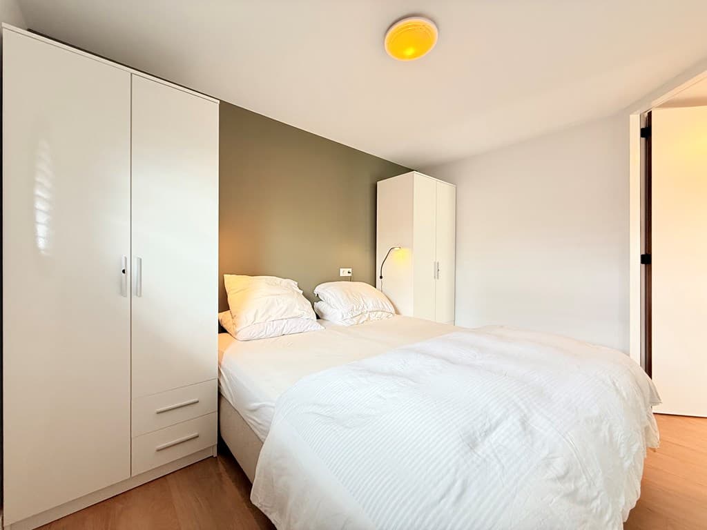 Slaapkamer met tweepersoonsbed, witte kast en zacht verlichte wand in een moderne inrichting