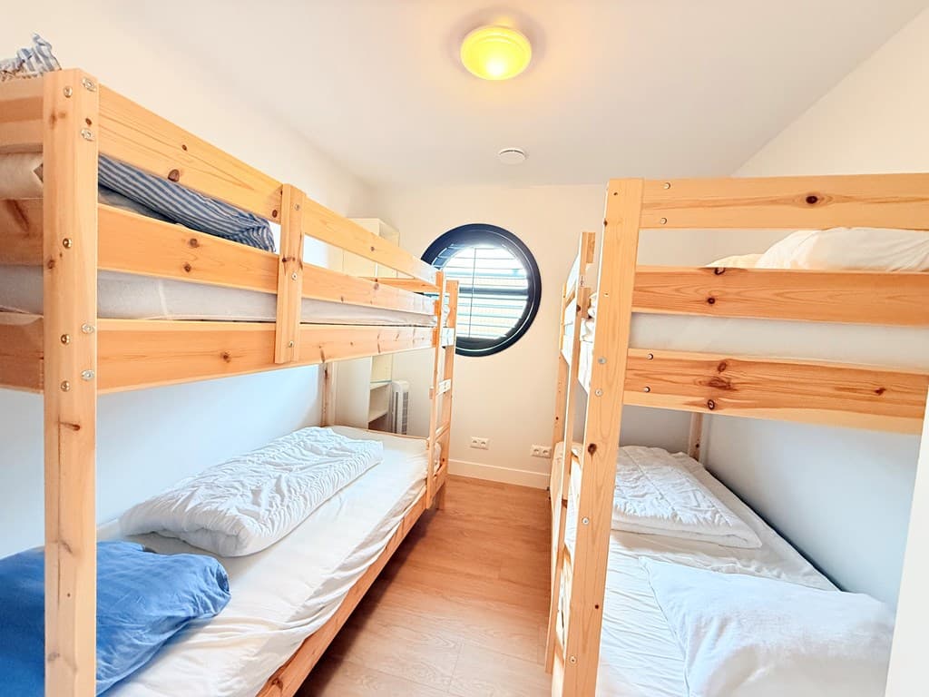 Slaapkamer met stapelbedden en ronde venster voor natuurlijk licht.
