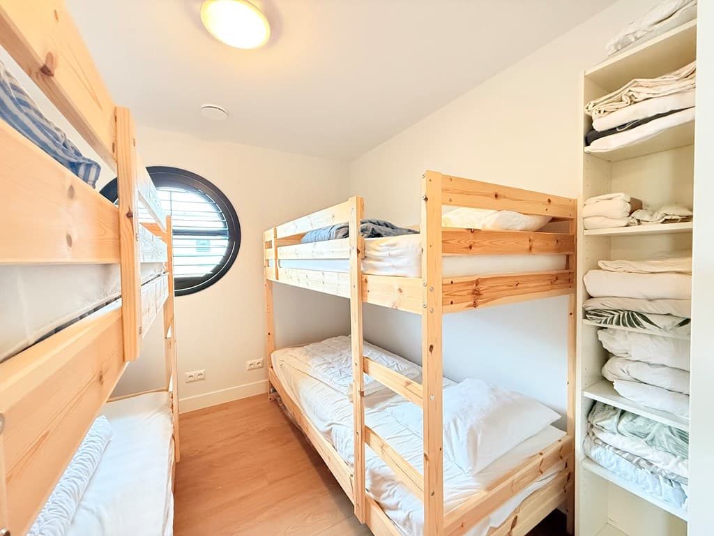 Slaapkamer met twee stapelbedden en een kledingkast gevuld met linnengoed, ronde raam zorgt voor natuurlijk licht
