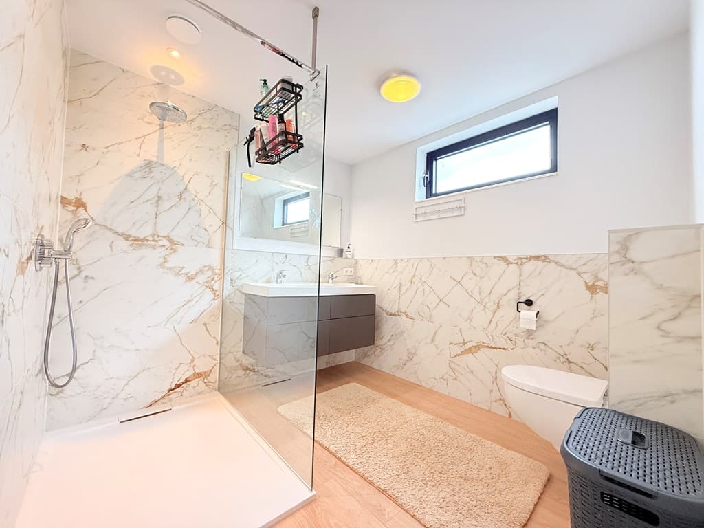 Moderne badkamer met marmeren wandtegels, inloopdouche en wastafel met opbergkast, voorzien van natuurlijk licht vanuit het r