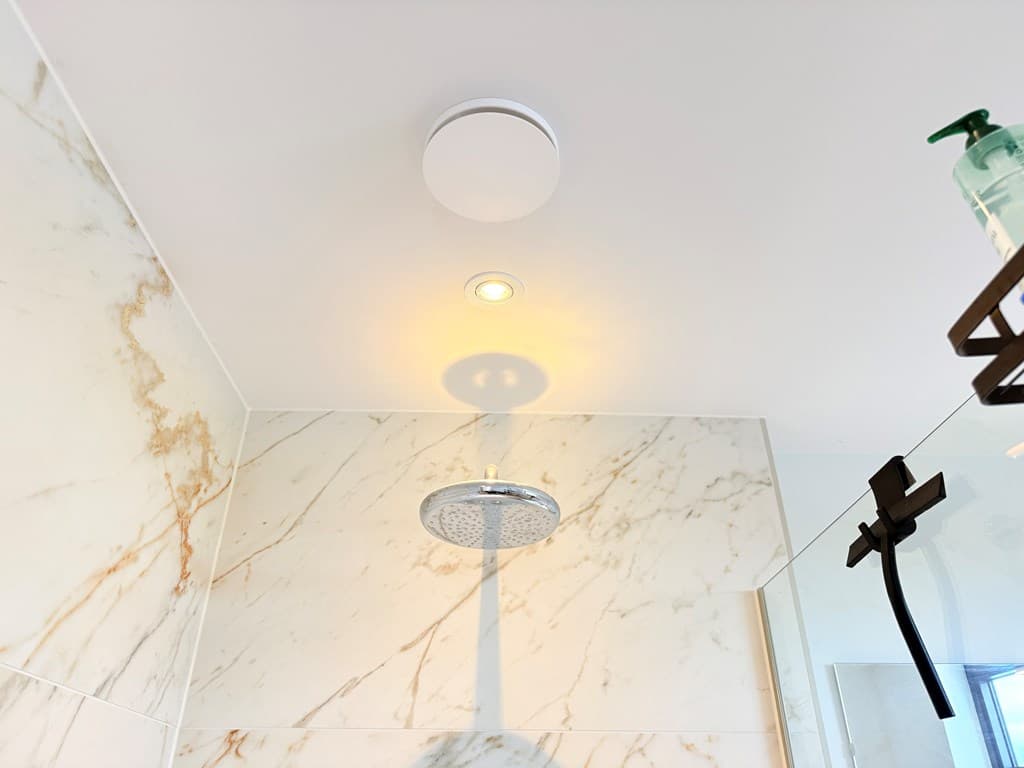 Moderne badkamer met marmeren wanden, inloopdouche en een plafondlamp.