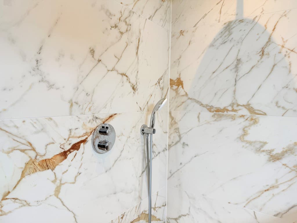Moderne douche met marmeren wandtegels met gouden aders en een chroomkleurige douchekop