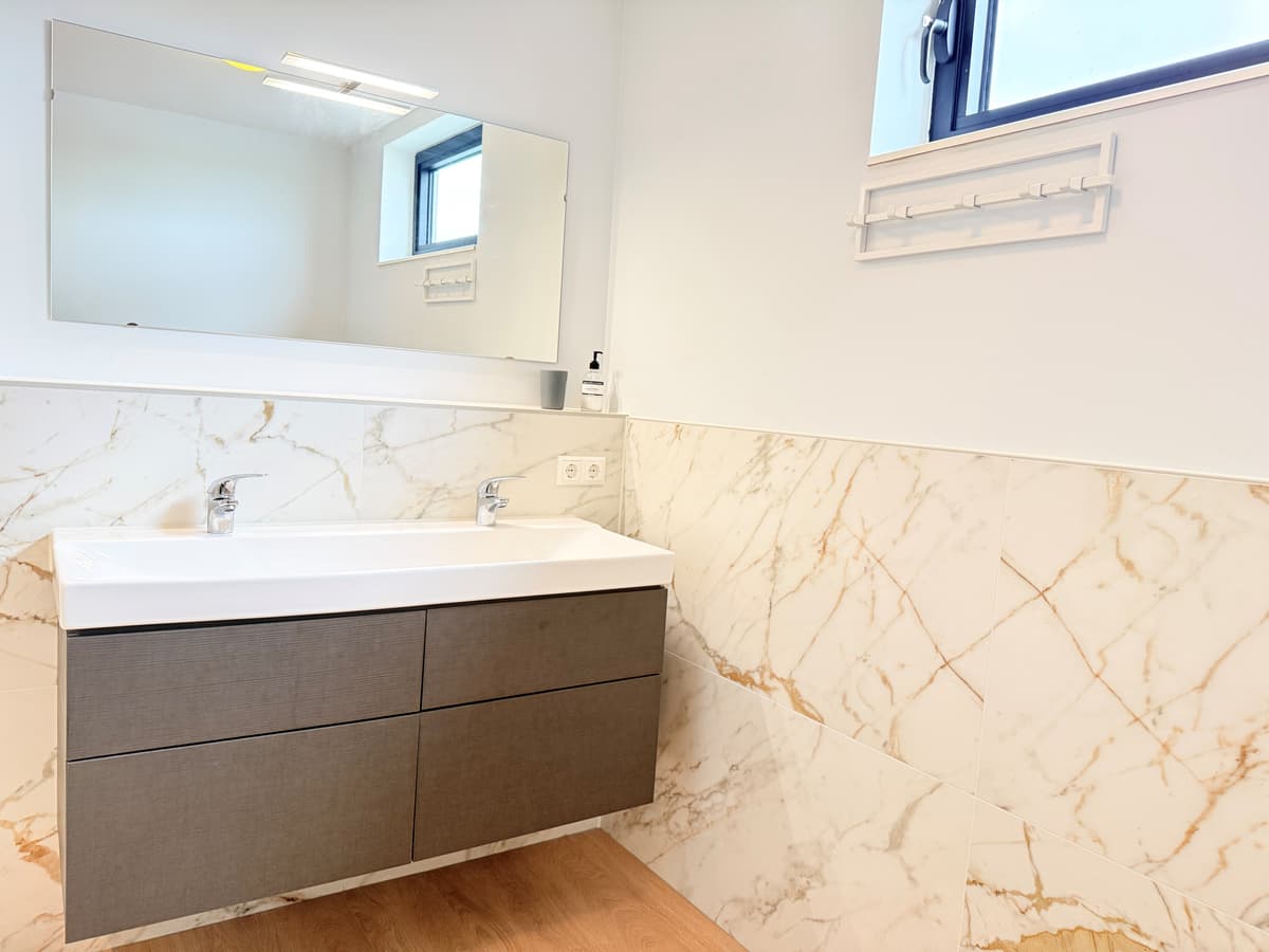 Moderne badkamer met marmeren wanden, een wandspiegel en een wastafel met lades.