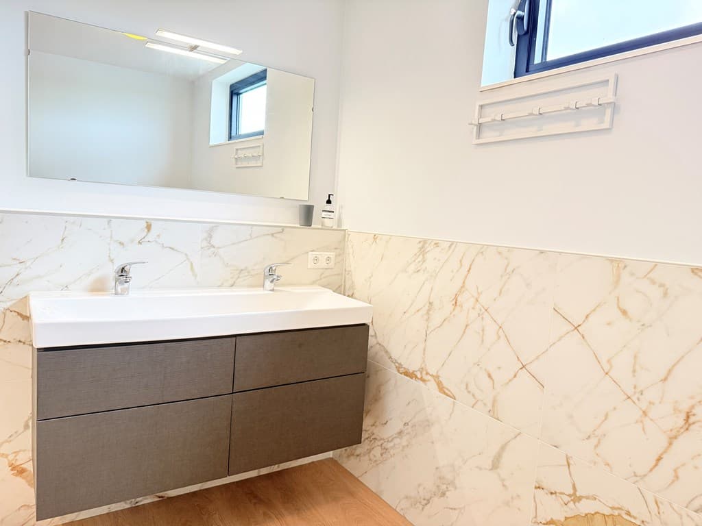 Moderne badkamer met marmeren wanden, een wandspiegel en een wastafel met lades.
