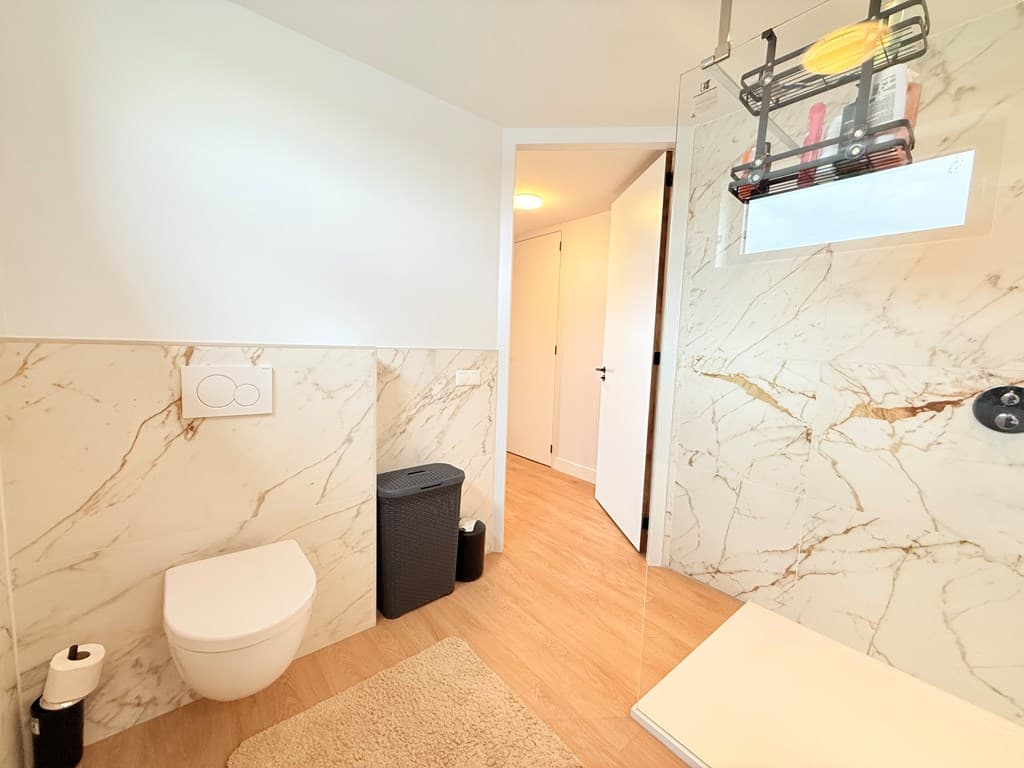 Moderne badkamer met marmeren muren, douche en toilet, met een deur naar een andere ruimte.