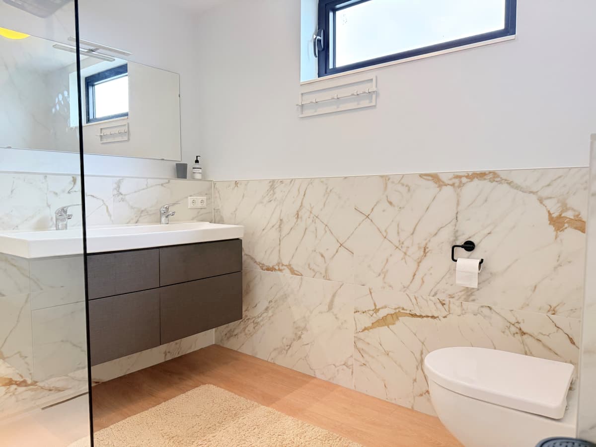 Moderne badkamer met marmerlook tegels, een wastafel met opbergruimte en een toilet tegen de wand.