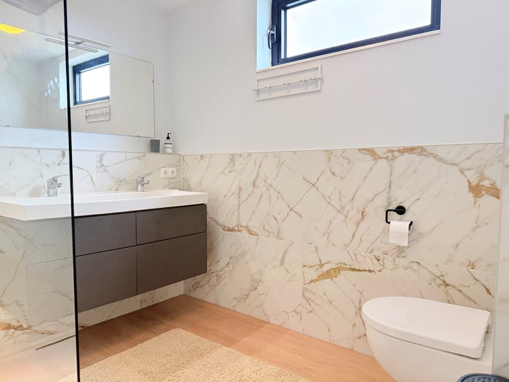 Moderne badkamer met marmerlook tegels, een wastafel met opbergruimte en een toilet tegen de wand.