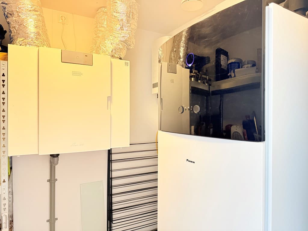 In de bijkeuken staan een koelkast en een vriezer naast elkaar, met ventilatiebuizen aan het plafond.