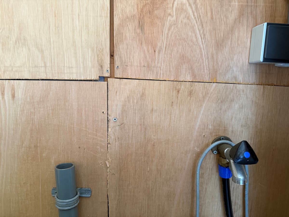 Houten wand met naden, een waterkraan en leidingen zichtbaar in de ruimte.
