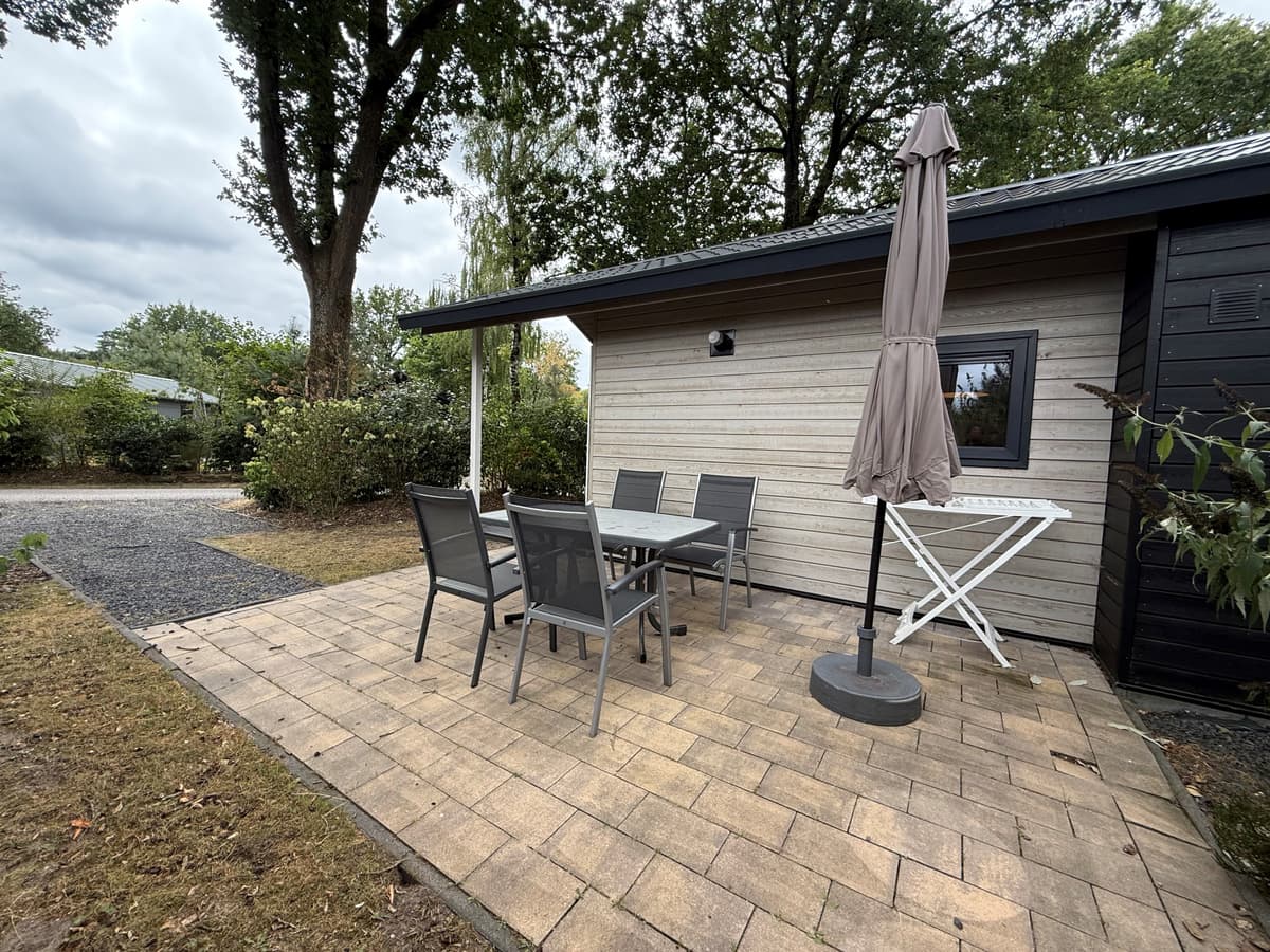 Terras met een eettafel en stoelen, parasol en een grindpad in de tuin van een vakantiehuis