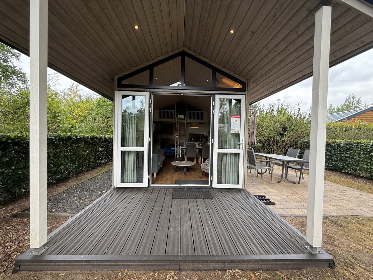 Buitenzicht op de woning met open deuren, houten terras en uitzicht op een tuin met stenen pad en meubels.