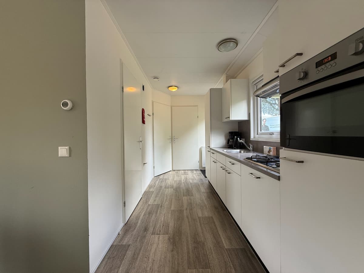 Moderne keuken met lichte kastjes, een lange werkbladcabinet en een deur naar een andere ruimte.