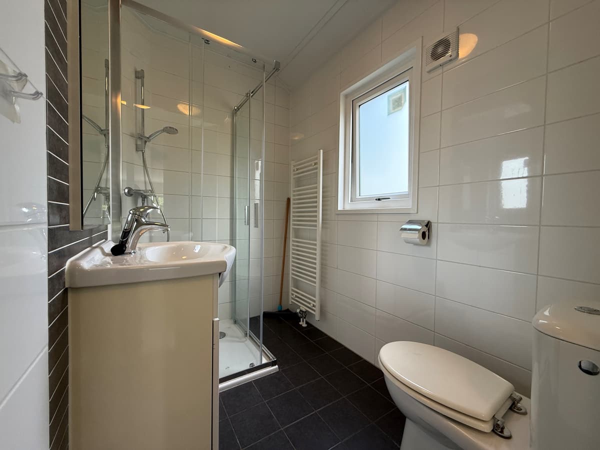 Moderne badkamer met inloopdouche, wastafel en toilet, betegelde wanden en donkergrijze vloertegels.