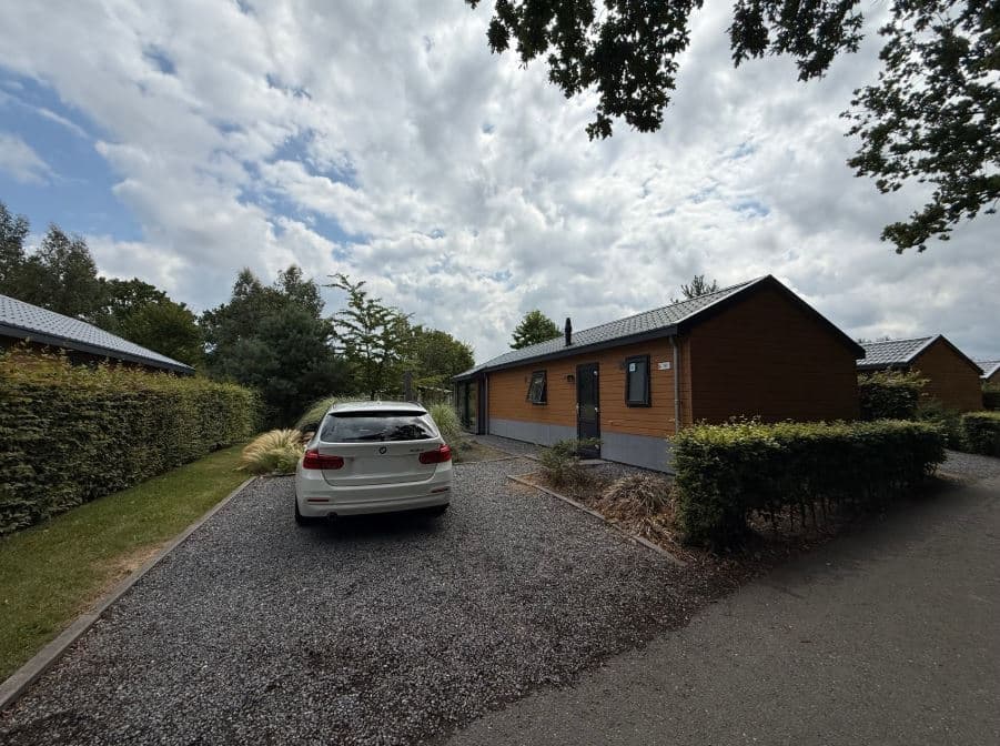 Buitenaanzicht van een woning met een wit voertuig op een grindpad, omgeven door groen en een goed onderhouden tuin