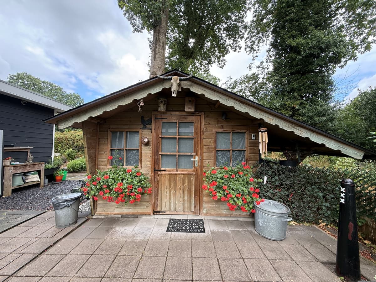 Houten recreatiewoning met bloemen en decoratieve elementen aan de voorzijde, omringd door groen en grindpaden