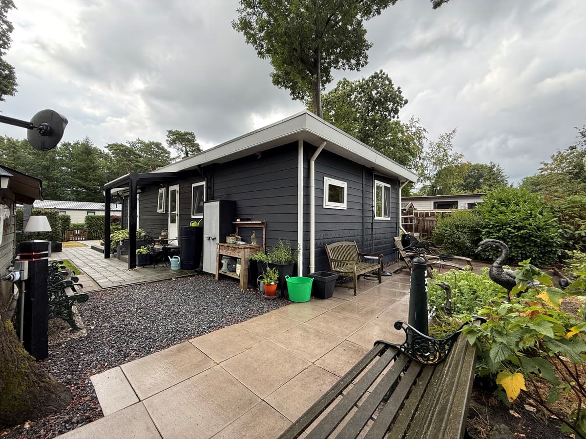 Zijaanzicht van een recreatiewoning met een betegeld terras, plantenbakken en een groene tuin rondom