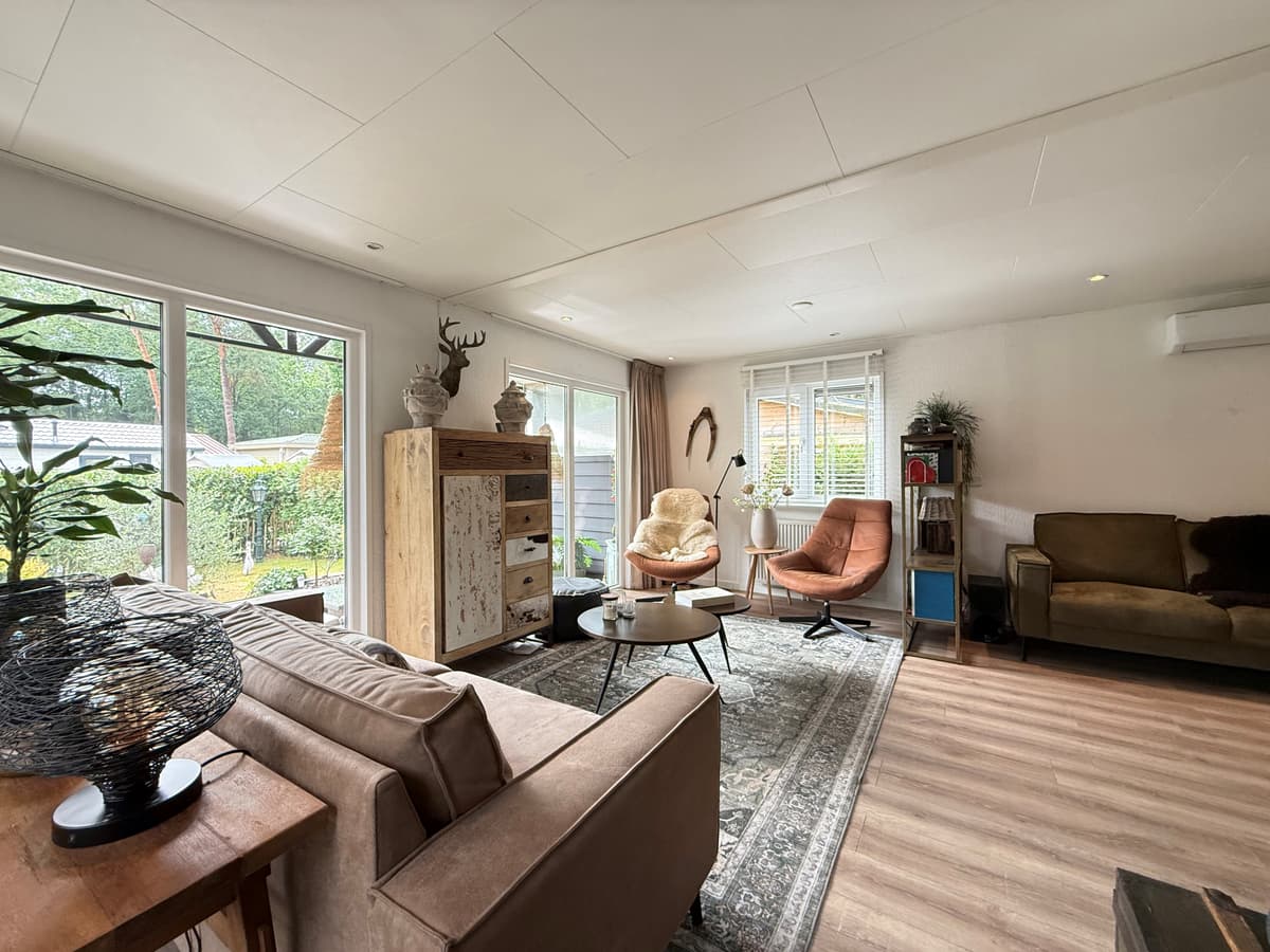 Ruim en licht interieur van een recreatiewoning met moderne meubels, grote ramen en een zithoek met verschillende stoelen