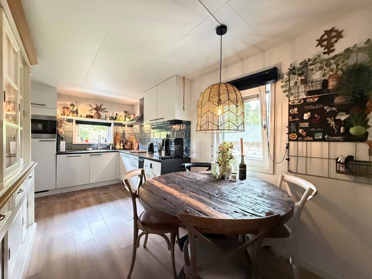 Gezellige keuken met een ronde houten eettafel, moderne apparatuur en wanddecoraties met planten en kruiden.