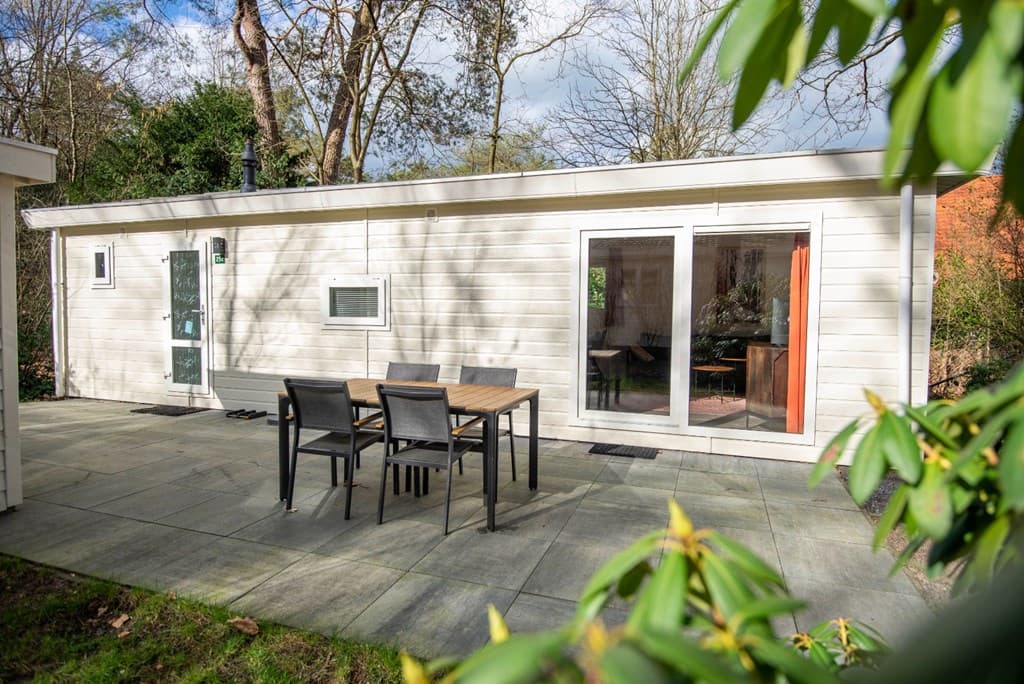 Moderne vakantiewoning met houten aanbouw, terras en eettafel met stoelen, omringd door groene vegetatie