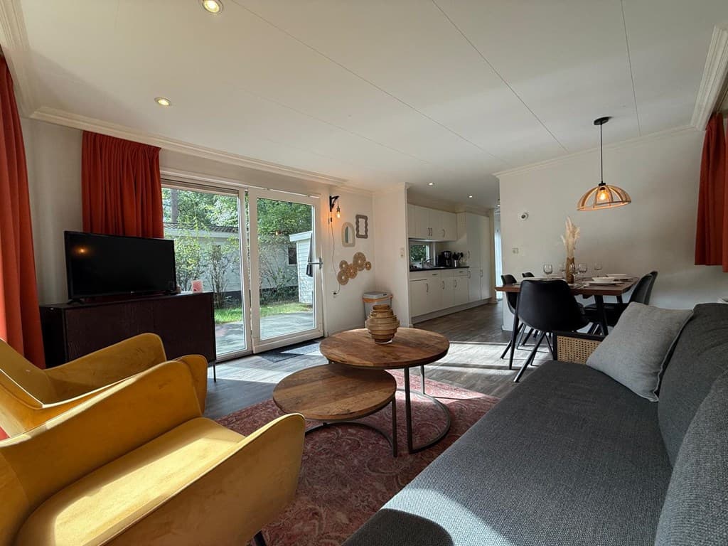 Woonkamer met kasten, een tv, een eettafel en uitzicht op de tuin door de glazen deuren.