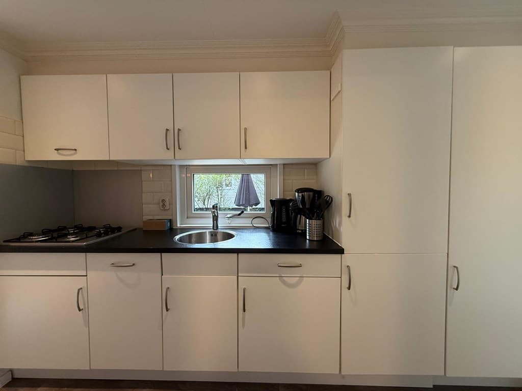 Moderne keuken met witte kasten, een gasfornuis, een wasbak en een koffiezetapparaat bij een raam met uitzicht.