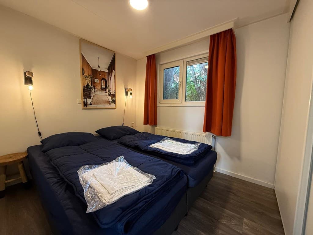 Slaapkamer met twee eenpersoonsbedden, nachtkastjes en een raam met oranje gordijnen.