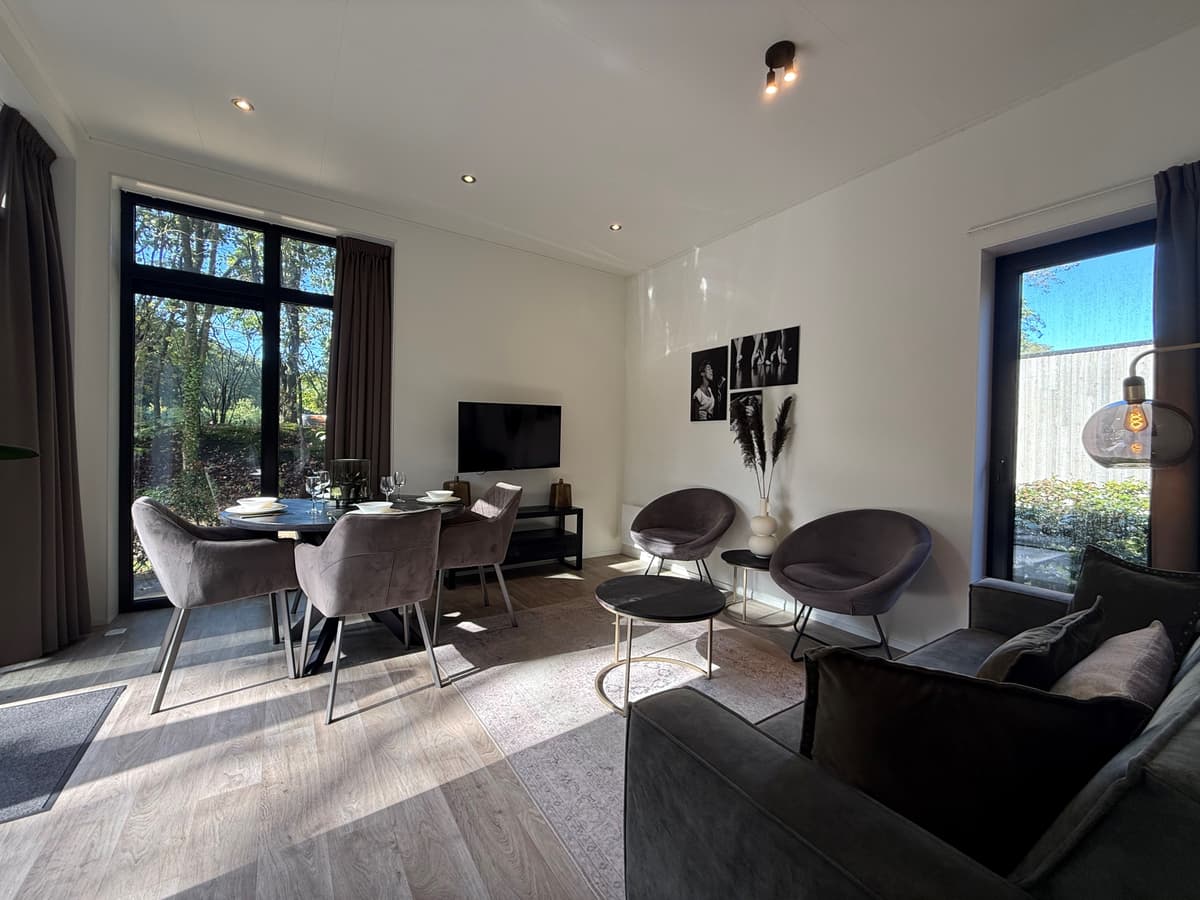 Licht woonkamer met een moderne inrichting, twee fauteuils, eettafel en grote ramen naar de tuin