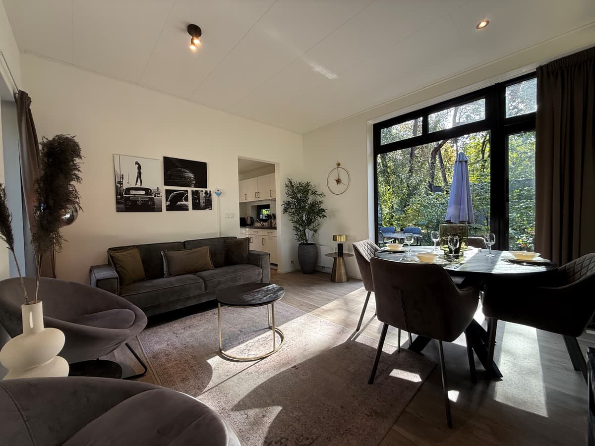 Moderne woonkamer met zithoek, eettafel en uitzicht op de groene omgeving door grote ramen