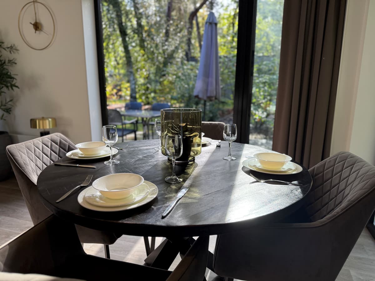 Eettafel met servies en glazen, uitzicht op groene omgeving door grote ramen met veel natuurlijk licht