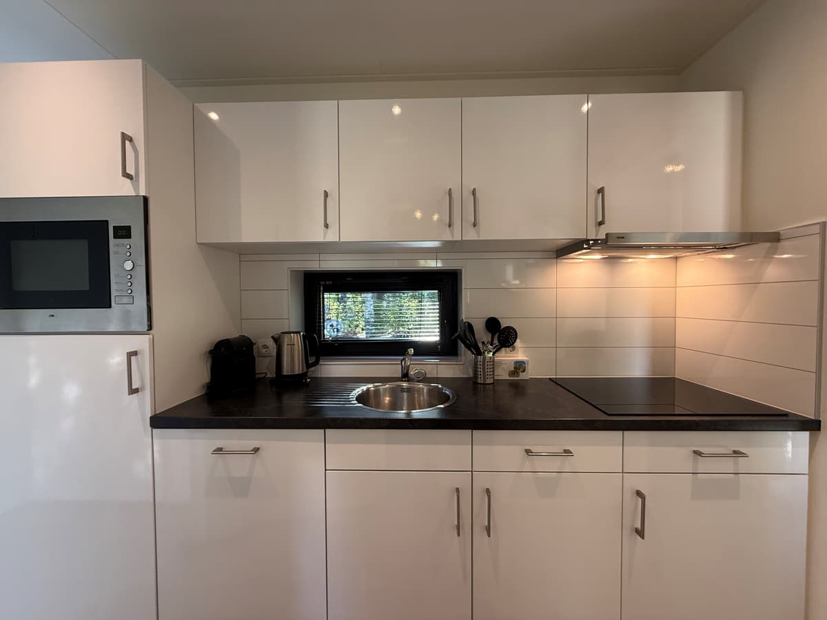 Moderne keuken met witte keukenkastjes, spoelbak, kookplaat en inbouwapparatuur zoals een magnetron en koffiezetapparaat
