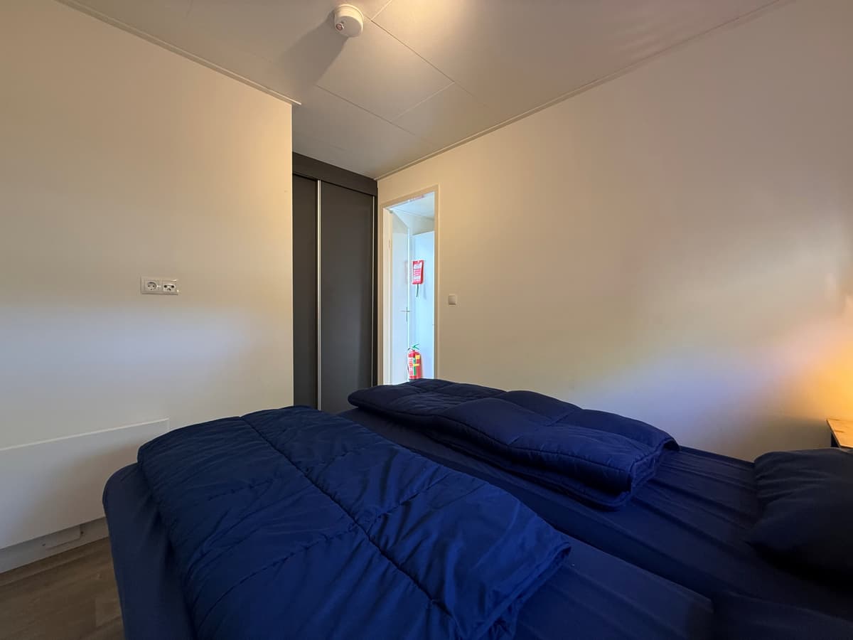 Slaapkamer met twee eenpersoonsbedden en een deur naar een gang met kast en verder toegang.