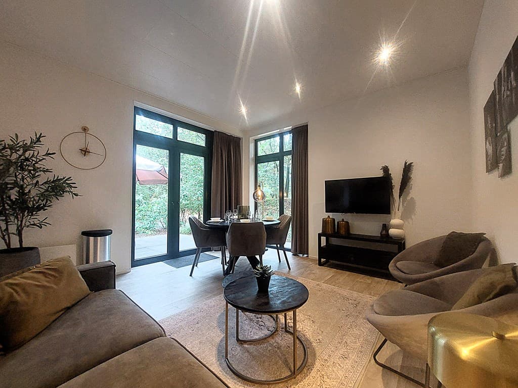 Moderne woonkamer met grote ramen, zitbank, fauteuils en eettafel, met uitzicht op de groene omgeving.
