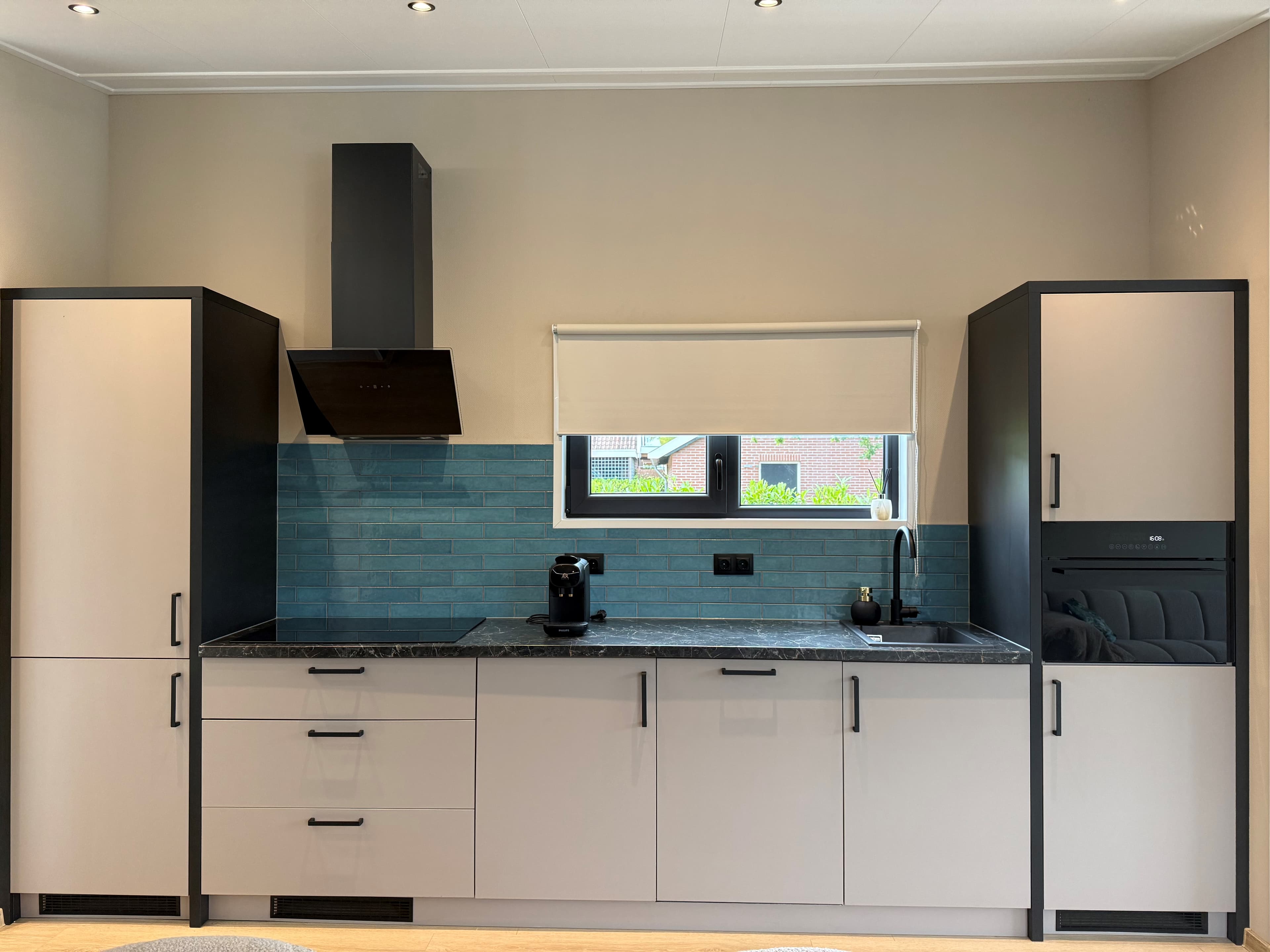 Moderne keuken met lichte kasten, zwart aanrechtblad en blauwe wandtegels, voorzien van kookplaat en inbouwapparatuur.