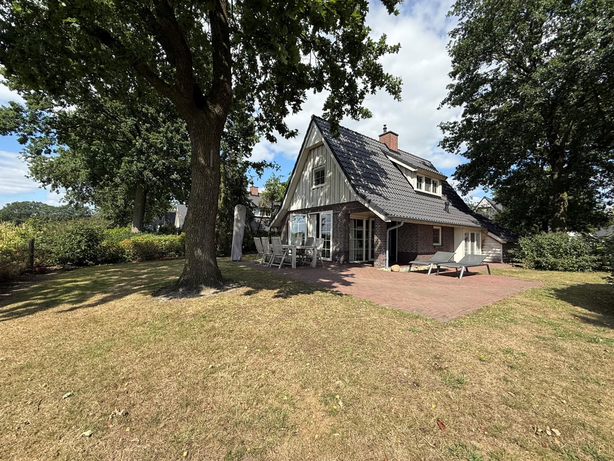 Recreatiewoning met een groen grasveld, terrassen, grote ramen en een houten gevel onder een hellend dak.