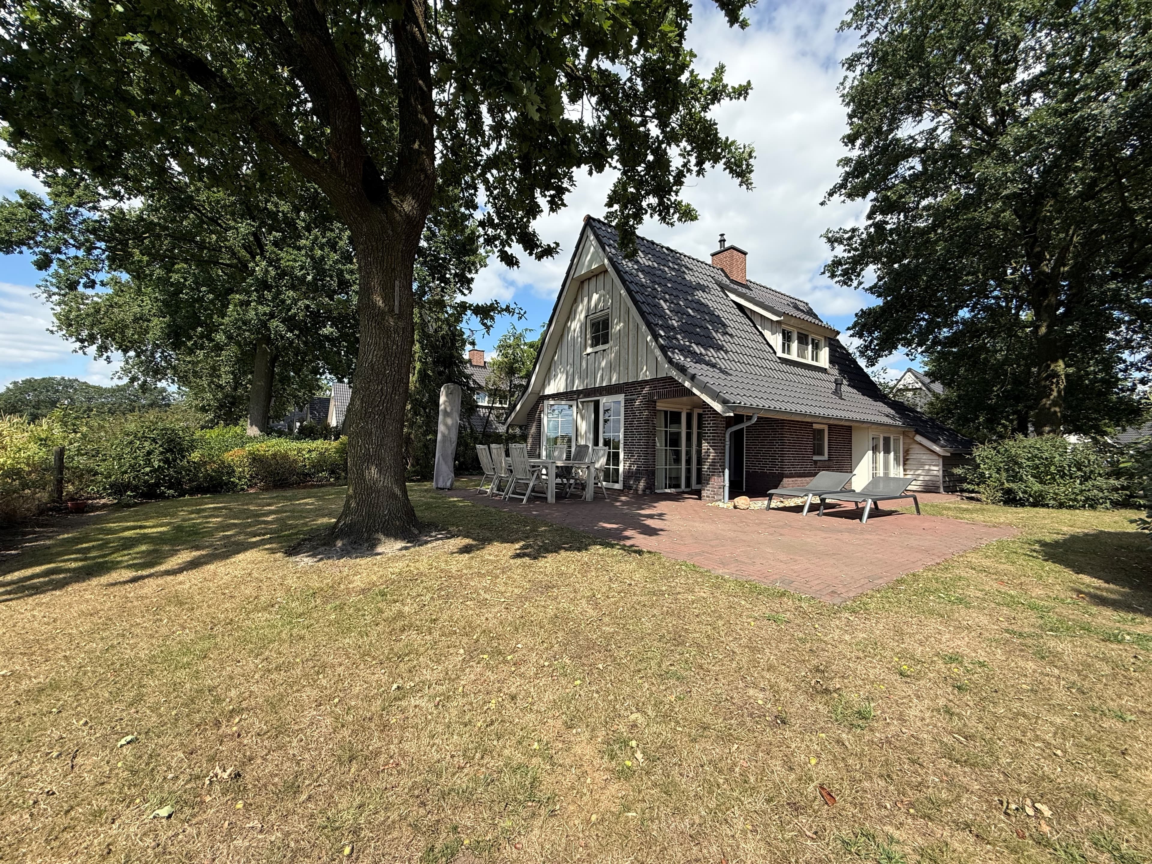 Recreatiewoning met een groen grasveld, terrassen, grote ramen en een houten gevel onder een hellend dak.