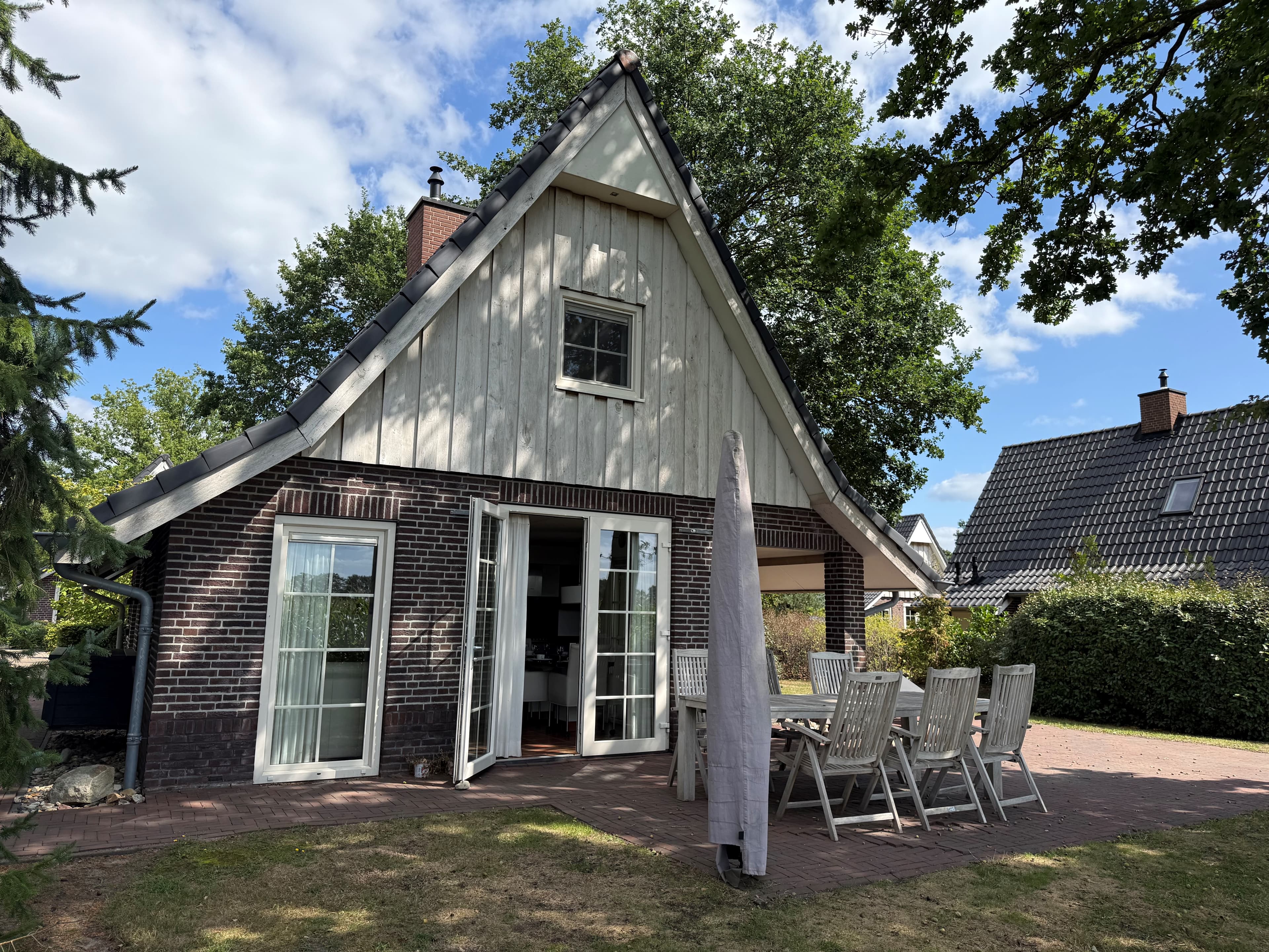 Recreatiewoning met een lichte gevel, grote ramen en een patio met tafel en stoelen, omringd door groen.
