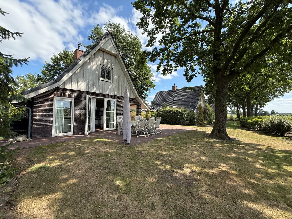 Recreatiewoning met een tuin, terras met tafel en stoelen, en omliggende bomen in een groene omgeving