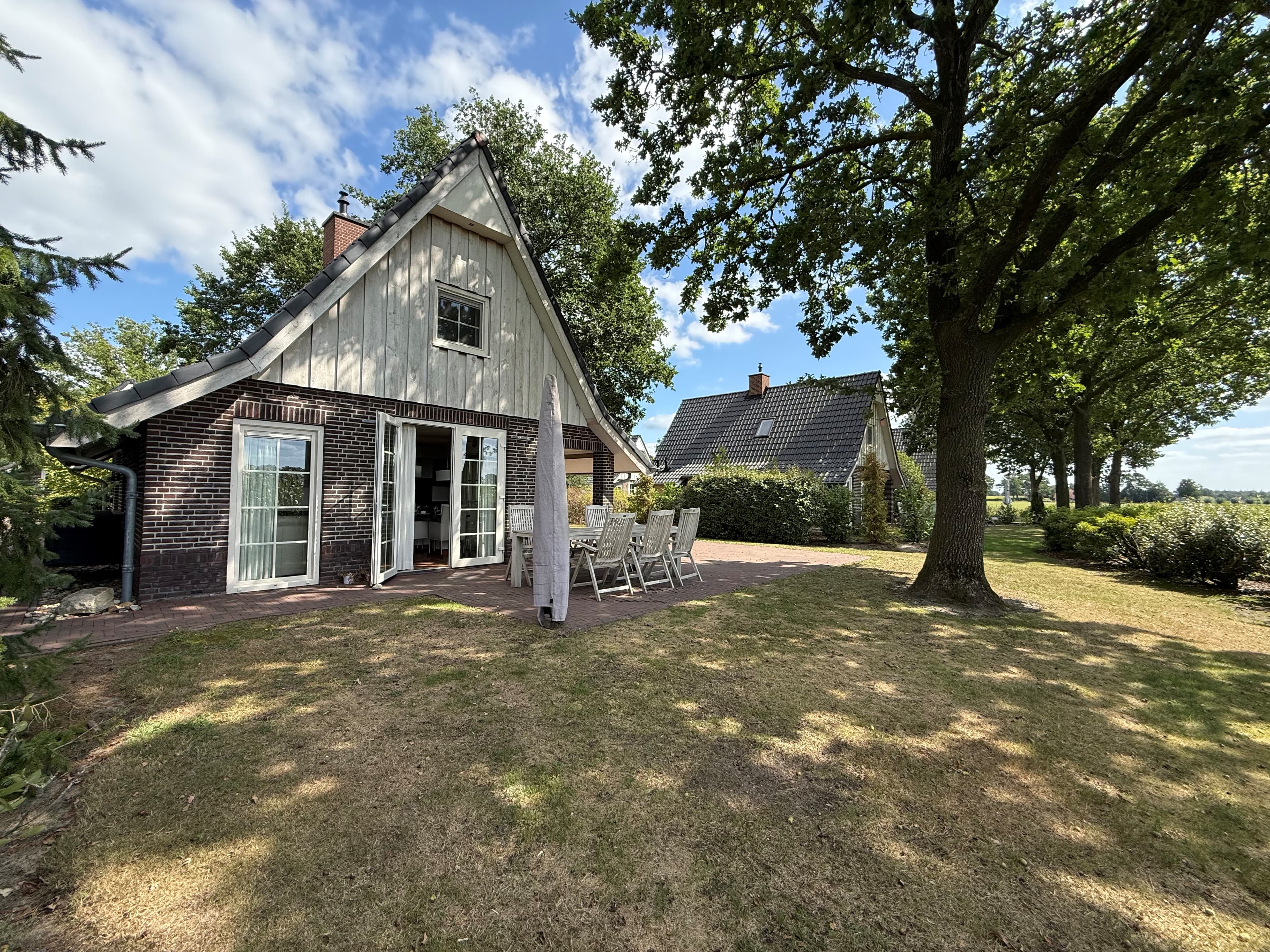 Recreatiewoning met een tuin, terras met tafel en stoelen, en omliggende bomen in een groene omgeving
