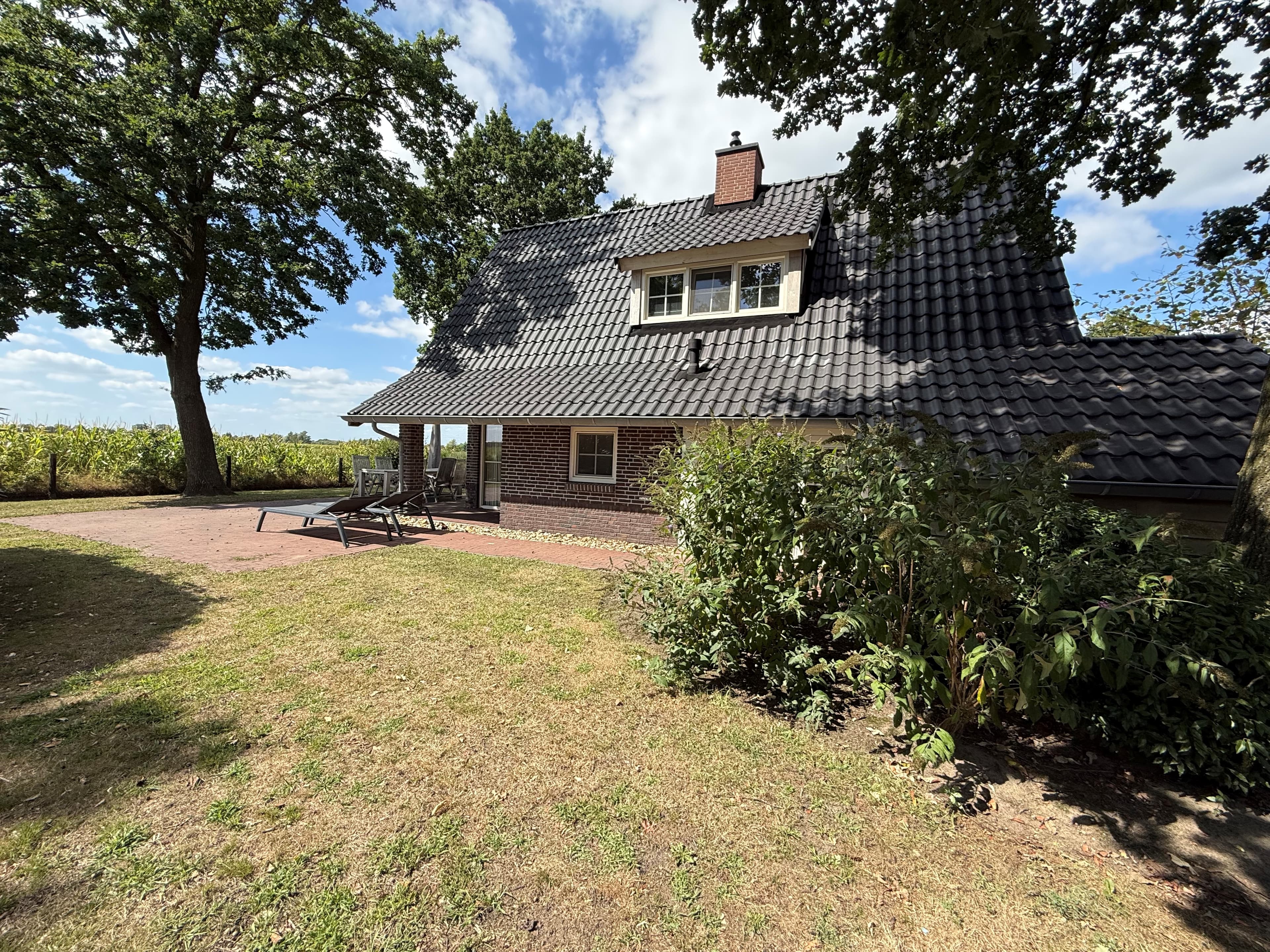 Twee-verdiepingen tellende recreatiewoning met een stenen gevel en houten dak, gelegen in een groene omgeving met gras en bom