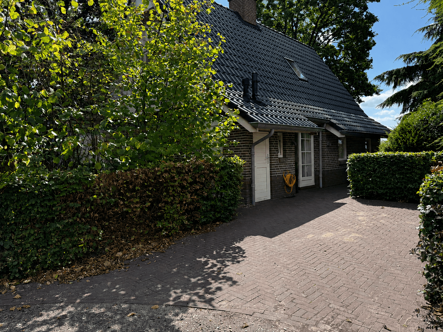 Twee-laags recreatiewoning met een betegeld pad, groene begroeiing en een dak met zwarte dakpannen