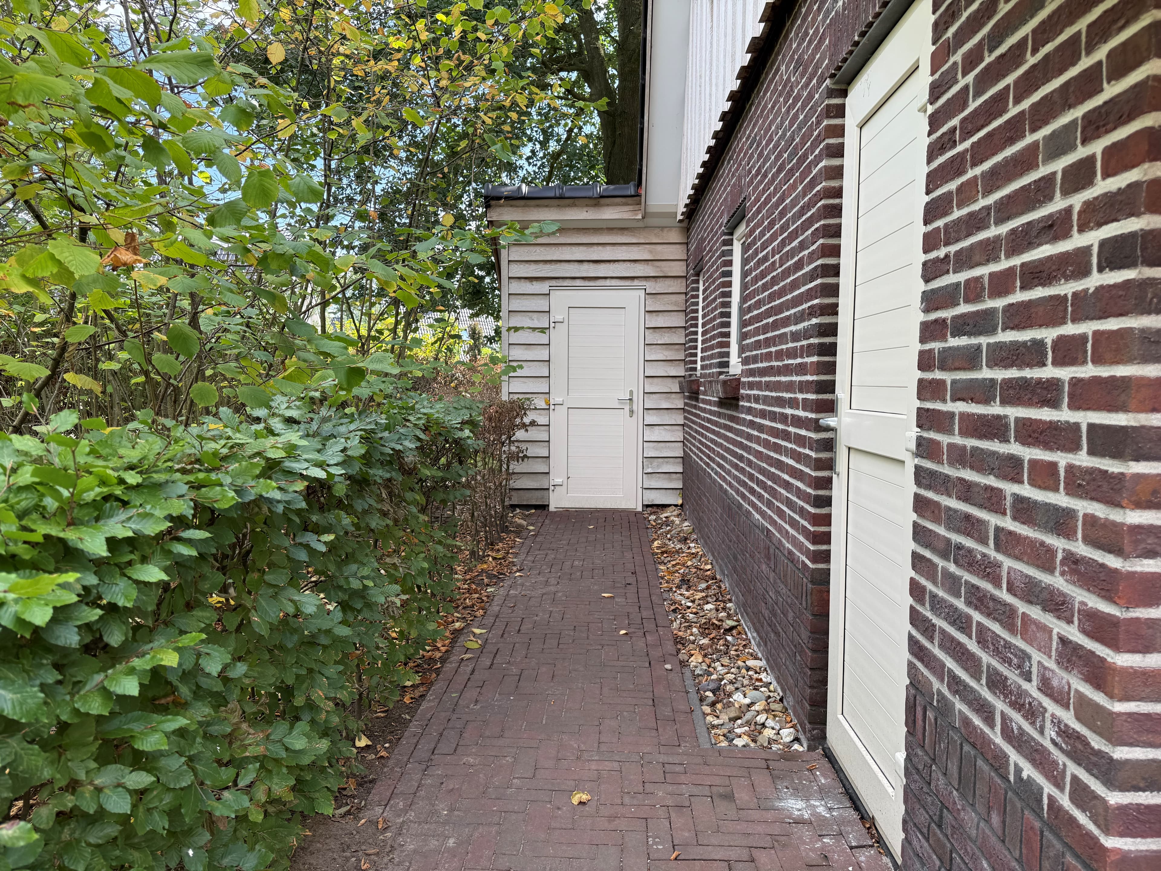 Zijaanzicht van een recreatiewoning met een betegeld pad en groene begroeiing aan de zijkant